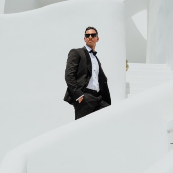 Groom wearing a black wool dinner suit and bow tie, photographed against a white wall during his Greek islands elopement.