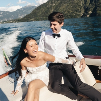 Groom in a black wool dinner shirt, bow tie, and trousers on a boat in Lake Como, jacket removed, relaxed formal travel look.
