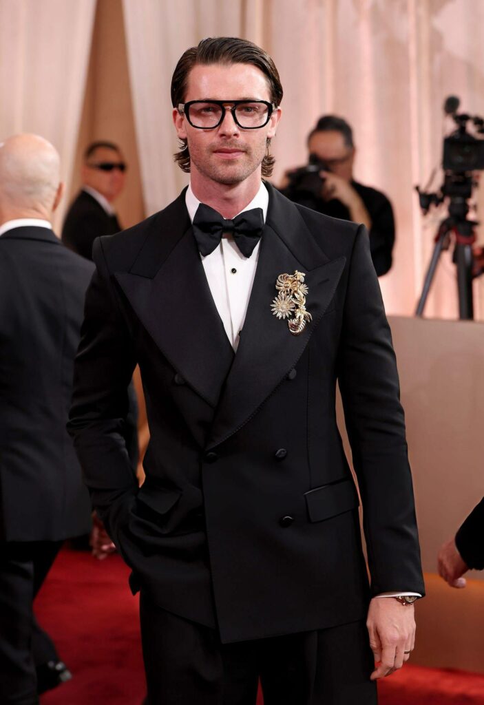 Patrick Schwarzenegger at the 2026 Golden Globes wearing a double-breasted peak lapel tuxedo with a giant butterfly bowtie and a brooch