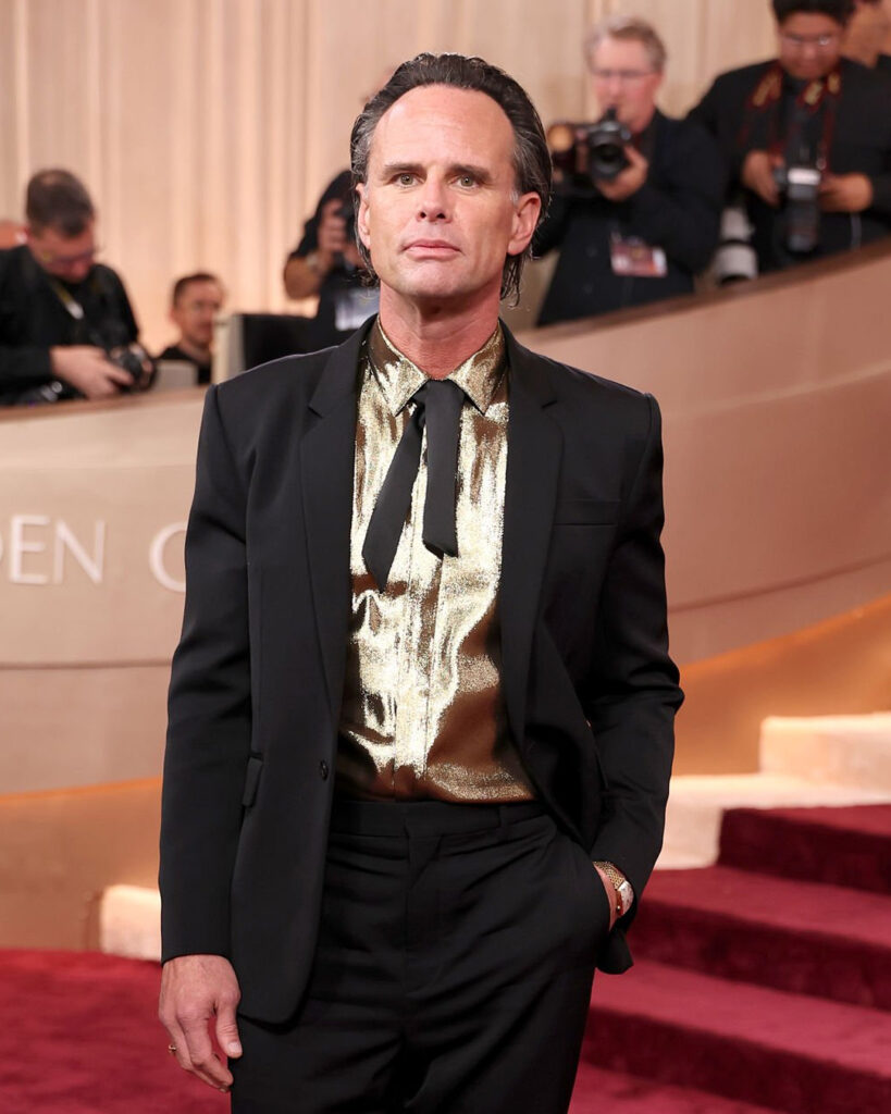 Walton Goggins at the 2026 Golden Globes wearing a black suit and gold shirt, paired with a string bowtie
